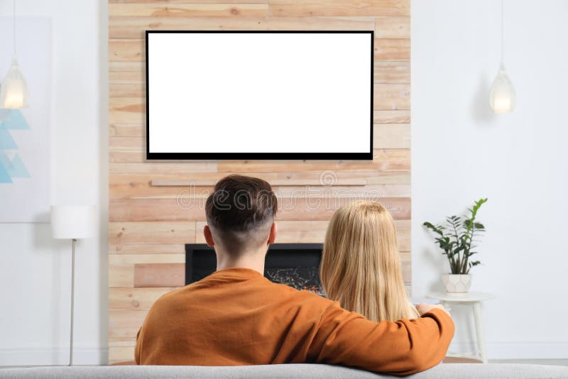 Couple watching TV on sofa in living room with decorative fireplace