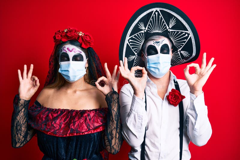 Couple wearing day of the dead costume wearing medical mask relax and smiling with eyes closed doing meditation gesture with