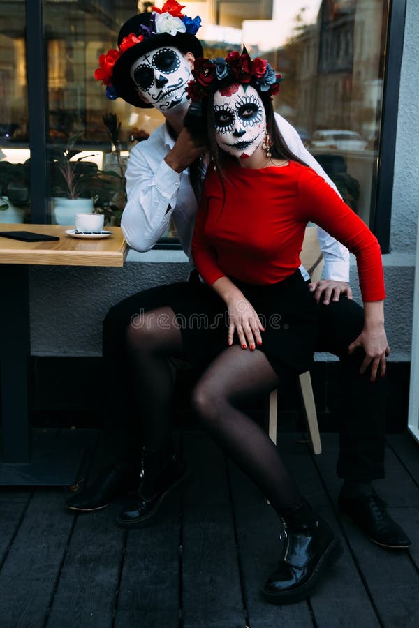 A couple, wearing skull make-up for. All souls day. Boy and girl sugar skull makeup.painted for halloween sit in a cafe. dead in t stock photo A couple, wearing skull make-up for. All souls day. Boy and girl sugar skull makeup.painted for halloween sit in a cafe. dead in t stock photo