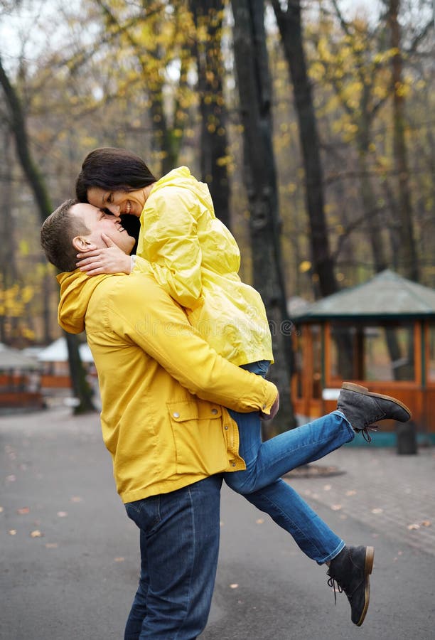 Couple in yellow jackets embracing and kissing, walking in the autumn park. Happy young family spends time together. royalty free stock photos Couple in yellow jackets embracing and kissing, walking in the autumn park. Happy young family spends time together. royalty free stock photos
