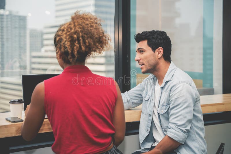 Couple of young designers working at modern office, two coworkers discussing fun project over a laptop, little team of stock images Couple of young designers working at modern office, two coworkers discussing fun project over a laptop, little team of stock images