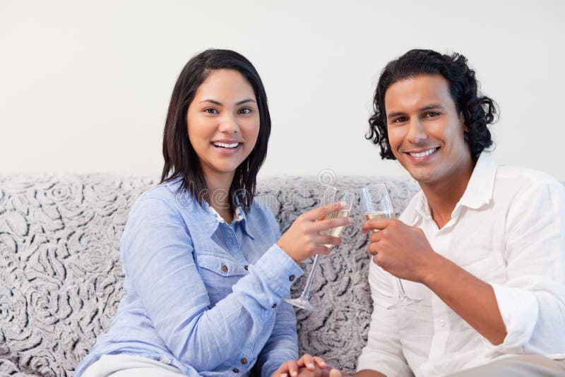 Couples ayant le vin mousseux sur le sofa image stock Couples ayant le vin mousseux sur le sofa image stock