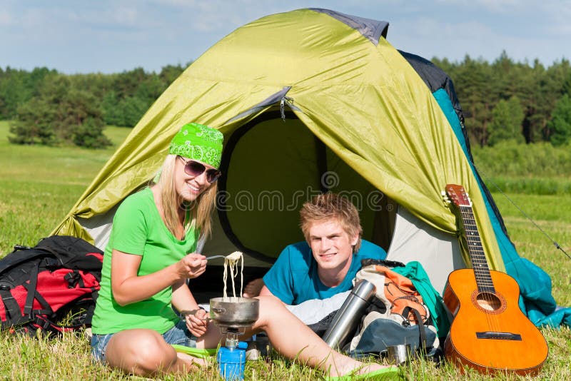 Couples campants de jeunes faisant cuire le repas en dehors de la tente images libres de droits Couples campants de jeunes faisant cuire le repas en dehors de la tente images libres de droits
