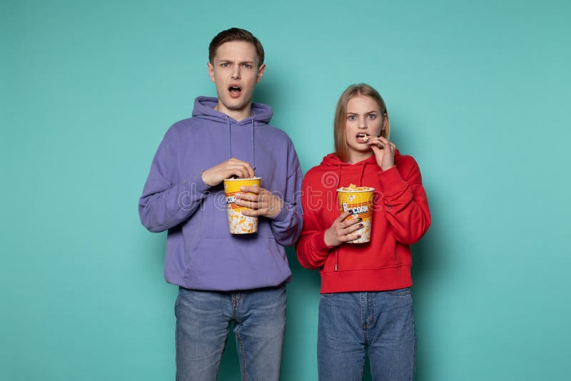Couples choqués outragés par jeunes dans des vêtements sport observant le film contradictoire, tenant le seau de maïs éclaté photo stock Couples choqués outragés par jeunes dans des vêtements sport observant le film contradictoire, tenant le seau de maïs éclaté photo stock