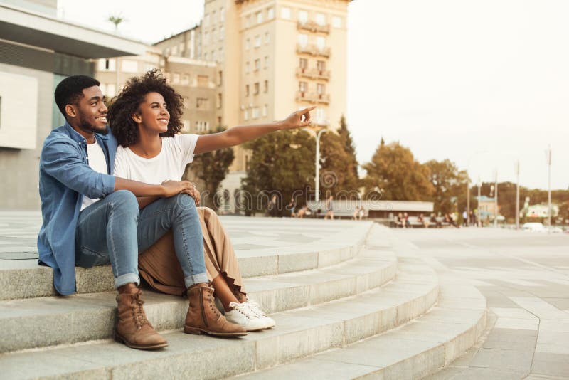 Look here. African-american couple of tourists walking in city, women pointing somewhere, copy space. Look here. African-american couple of tourists walking in city, women pointing somewhere, copy space