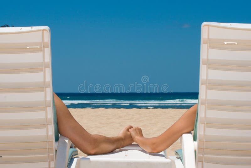 Couples dans des présidences de plage retenant des mains images stock Couples dans des présidences de plage retenant des mains images stock