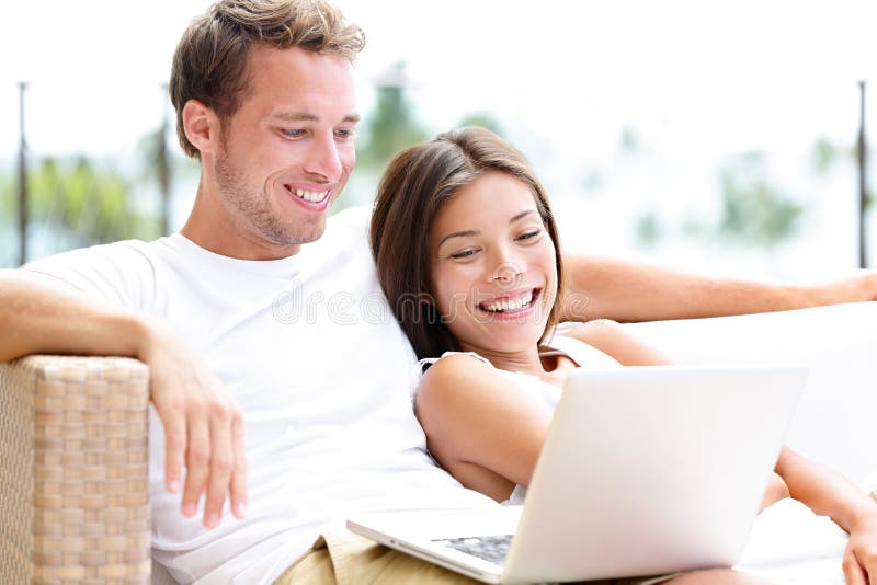 Couples dans le sofa avec le PC d'ordinateur portable à la maison riant images stock Couples dans le sofa avec le PC d'ordinateur portable à la maison riant images stock