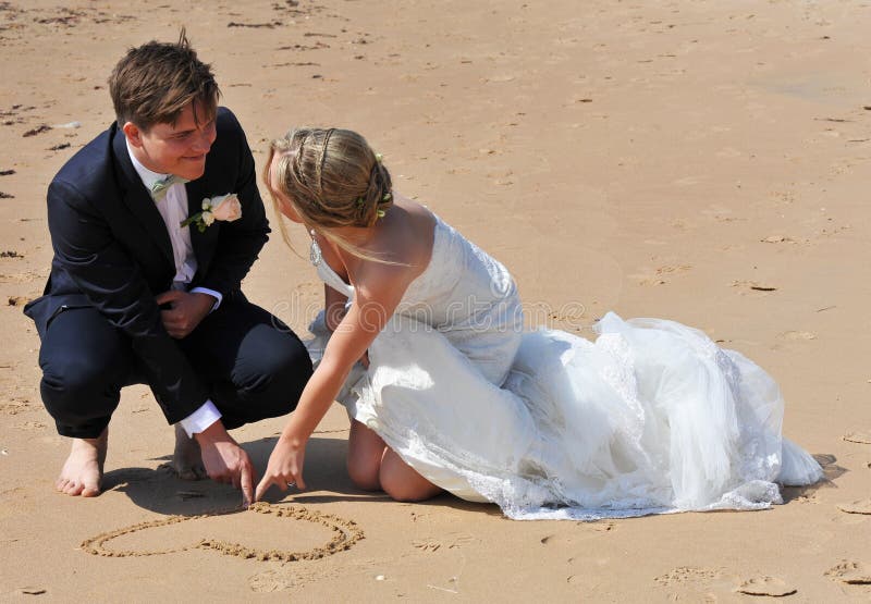 Couples de mariage dessinant un coeur dans le sable. photo stock Couples de mariage dessinant un coeur dans le sable. photo stock