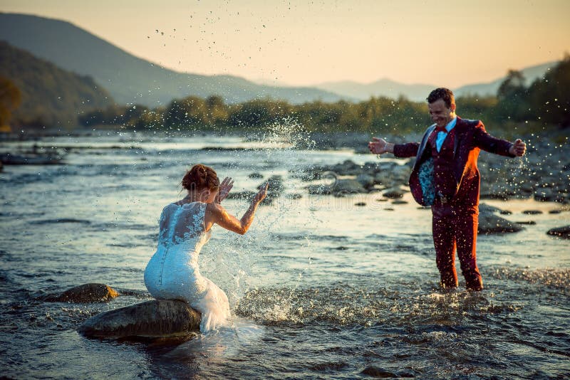 Couples de sourire heureux extérieurs émotifs de nouveaux mariés de portrait de mariage beaux jouant éclaboussant l'eau ayant le