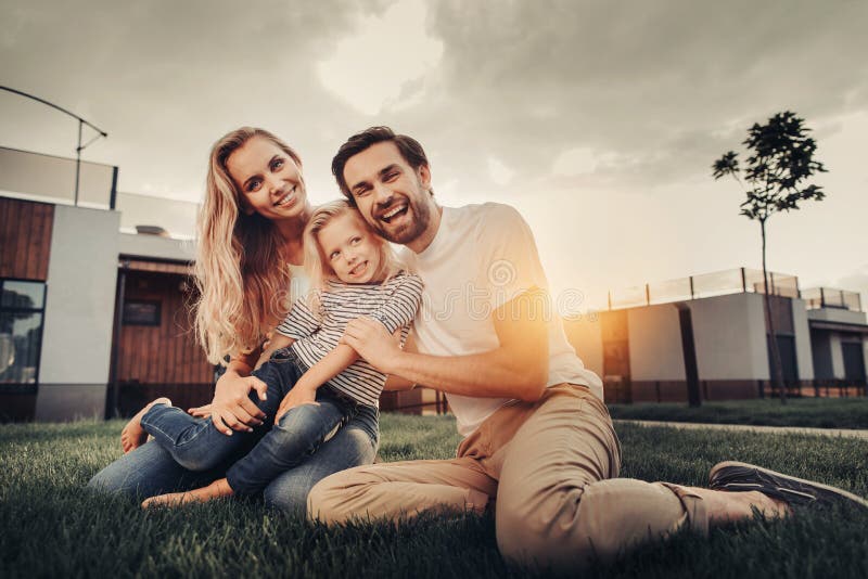 Couples de sourire étreignant l'enfant gai pendant le coucher du soleil photo stock Couples de sourire étreignant l'enfant gai pendant le coucher du soleil photo stock