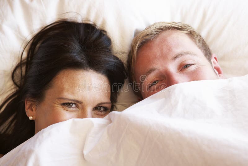 Couples détendant dans le lit se cachant sous la literie photographie stock Couples détendant dans le lit se cachant sous la literie photographie stock