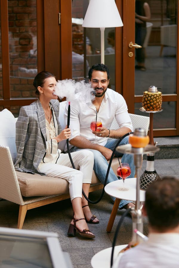Couples fumant Shisha et buvant des cocktails dans la barre de narguilé photographie stock libre de droits Couples fumant Shisha et buvant des cocktails dans la barre de narguilé photographie stock libre de droits