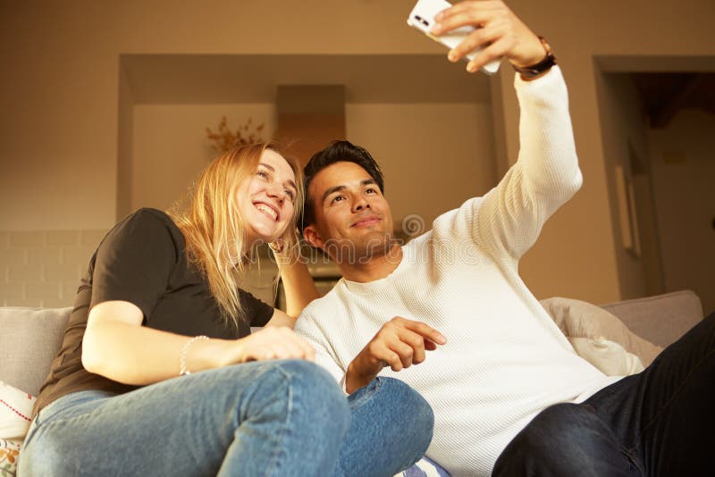 Couples heureux gais aimants prenant le selfie sur le sofa à la maison images stock Couples heureux gais aimants prenant le selfie sur le sofa à la maison images stock