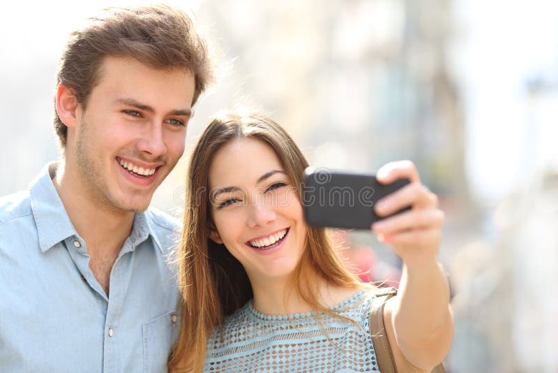 Couples heureux prenant des selfies utilisant le téléphone dans la rue photographie stock Couples heureux prenant des selfies utilisant le téléphone dans la rue photographie stock