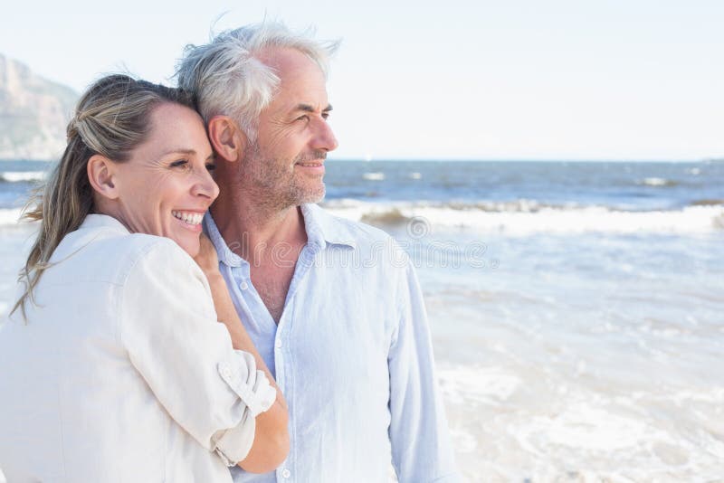 Couples heureux étreignant sur la plage regardant à la mer images stock Couples heureux étreignant sur la plage regardant à la mer images stock