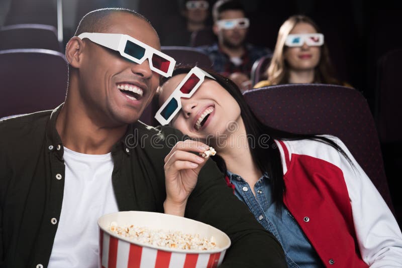 happy interracial couple in 3d glasses eaying popcorn and watching movie in cinema. happy interracial couple in 3d glasses eaying popcorn and watching movie in cinema