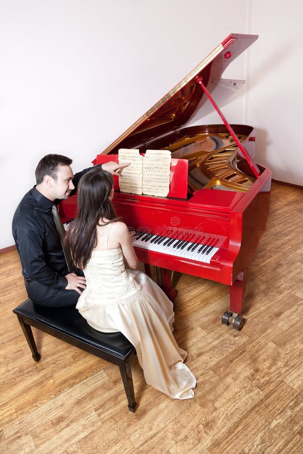 Couples jouant le piano rouge photographie stock libre de droits Couples jouant le piano rouge photographie stock libre de droits