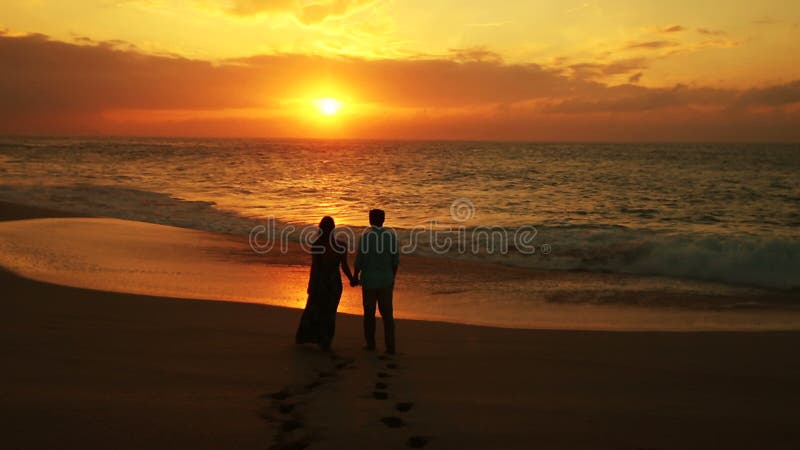 Couples marchant sur la plage appréciant des vacances de coucher du soleil sur le voyage romantique de lune de miel