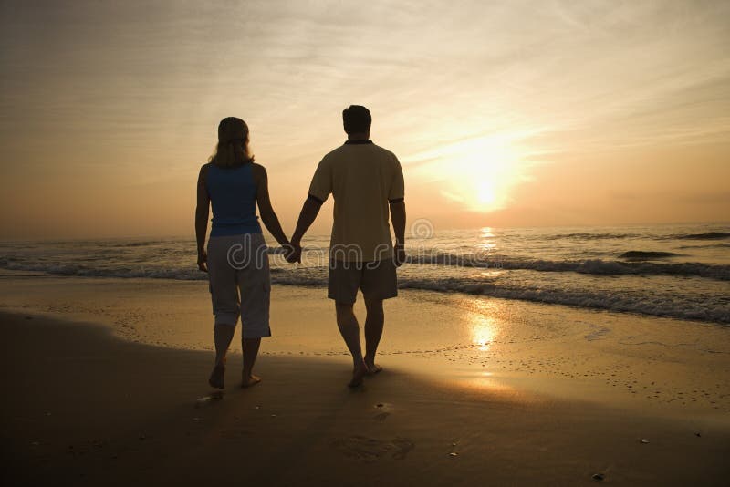 Couples marchant sur la plage au coucher du soleil