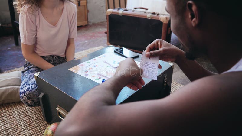 Couples multi-ethniques heureux dans des pyjamas jouant le jeu de société sur le plancher Équipez les jets découpent et mettent l photo libre de droits Couples multi-ethniques heureux dans des pyjamas jouant le jeu de société sur le plancher Équipez les jets découpent et mettent l photo libre de droits