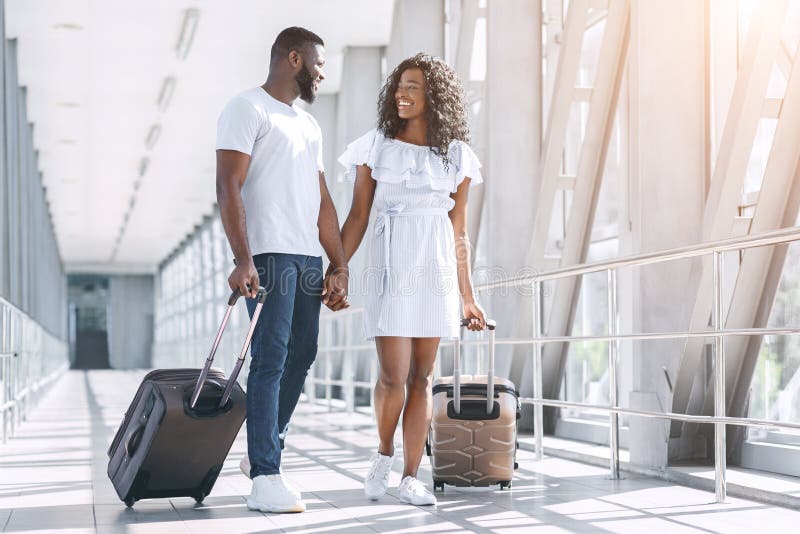 Couples noirs affectueux profitant du voyage de lune de miel en marchant avec des valises dans l'aéroport
