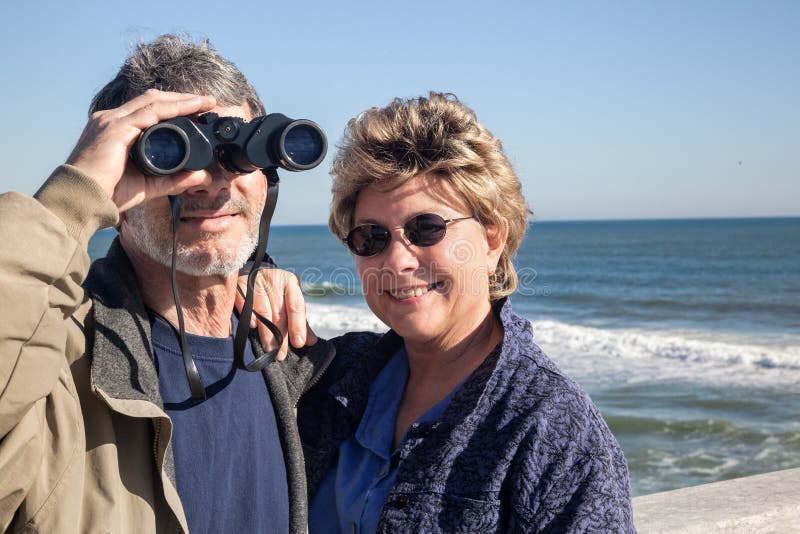Couples retirés des vacances de plage avec des jumelles image stock Couples retirés des vacances de plage avec des jumelles image stock