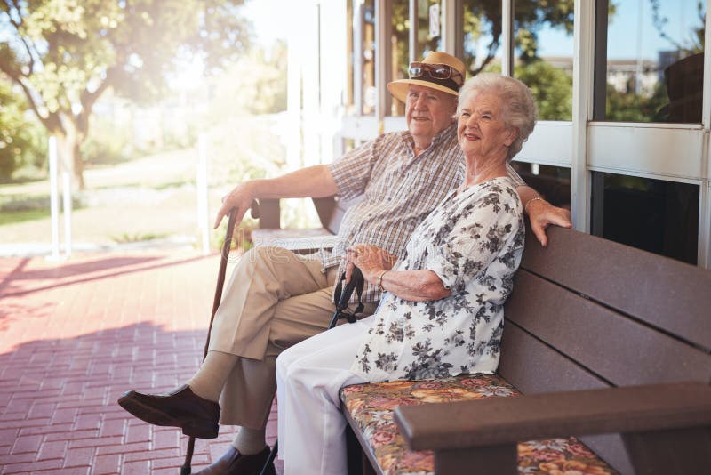 Couples retirés se reposant sur un banc en dehors de leur maison photographie stock libre de droits Couples retirés se reposant sur un banc en dehors de leur maison photographie stock libre de droits