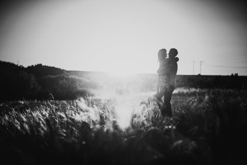 Couples romantiques de photographie blanche noire se tenant et embrassant sur le pré d'été de fond images stock Couples romantiques de photographie blanche noire se tenant et embrassant sur le pré d'été de fond images stock