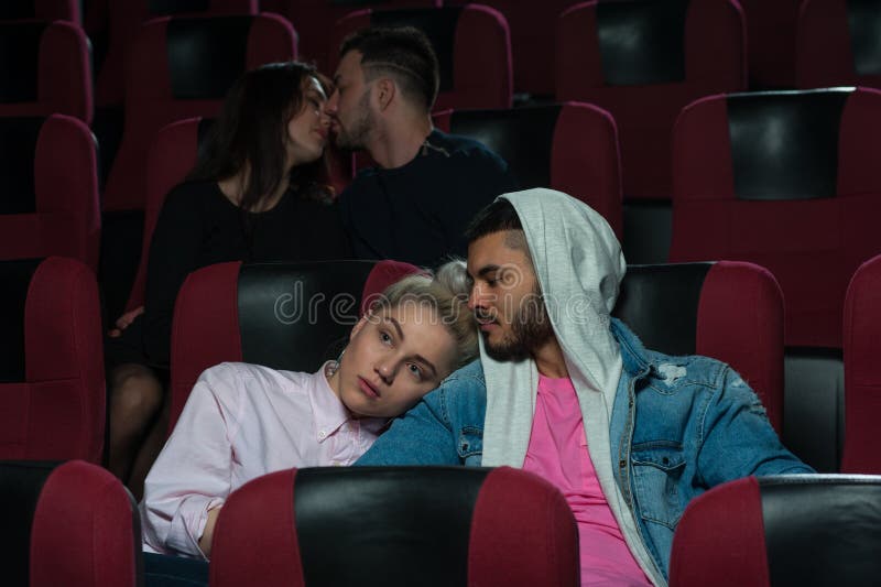 Group of young european adults watching movie in theater. Happy romantic couples in film session. Couple in love foreground sitting and hugging while another two kissing. Cinema, entertainment and leisure concept. Group of young european adults watching movie in theater. Happy romantic couples in film session. Couple in love foreground sitting and hugging while another two kissing. Cinema, entertainment and leisure concept.