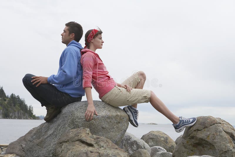 Couples se reposant de nouveau au dos sur des roches contre l'océan photos libres de droits Couples se reposant de nouveau au dos sur des roches contre l'océan photos libres de droits