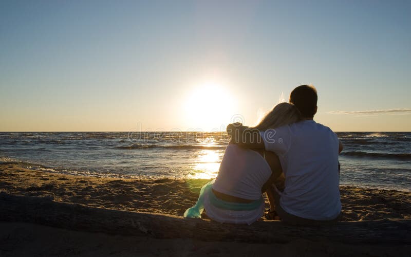Couples se reposant près de la mer sur le coucher du soleil photographie stock libre de droits Couples se reposant près de la mer sur le coucher du soleil photographie stock libre de droits
