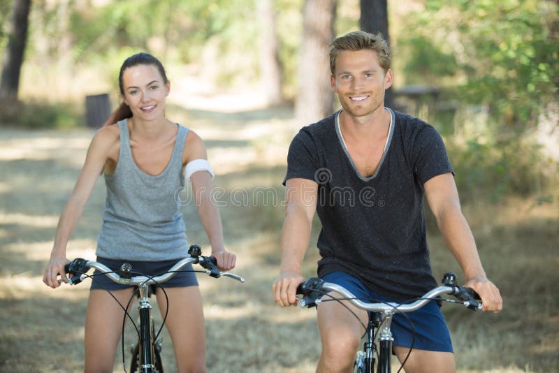 Couples sportifs de sourire faisant un cycle dans la forêt photo stock Couples sportifs de sourire faisant un cycle dans la forêt photo stock