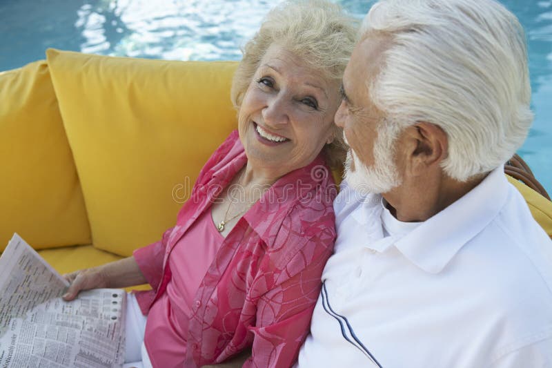 Couples supérieurs détendant par la piscine photo stock Couples supérieurs détendant par la piscine photo stock