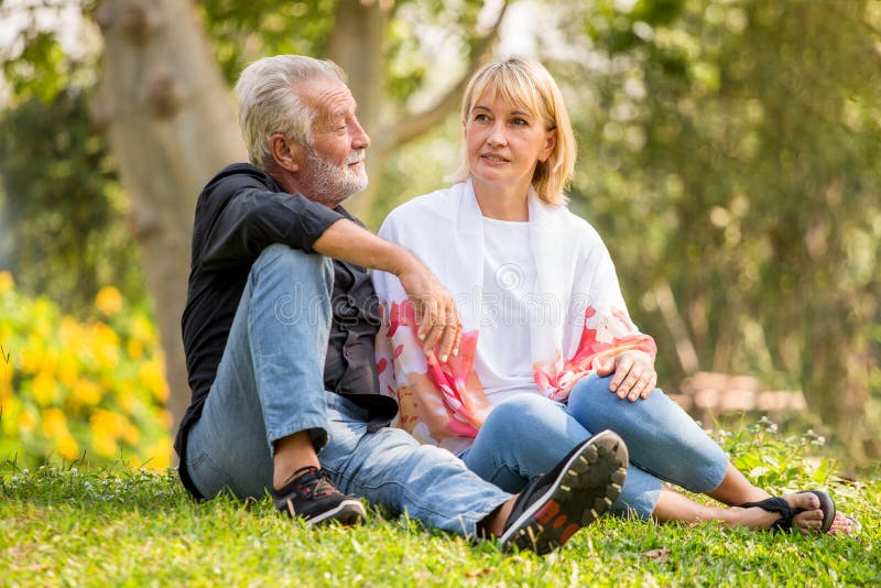 Couples supérieurs heureux détendant au parc ensemble dans le temps de matin personnes âgées s'asseyant sur l'herbe en parc d'aut