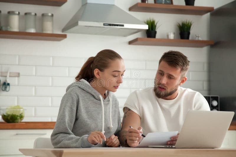 Couples sérieux focalisés vérifiant des factures se reposant ensemble au kitche photographie stock libre de droits Couples sérieux focalisés vérifiant des factures se reposant ensemble au kitche photographie stock libre de droits