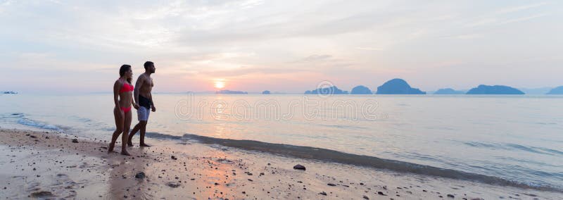 Couples tenant des mains marchant sur la plage au coucher du soleil, au jeune homme de touristes et à la femme des vacances de me photos stock Couples tenant des mains marchant sur la plage au coucher du soleil, au jeune homme de touristes et à la femme des vacances de me photos stock
