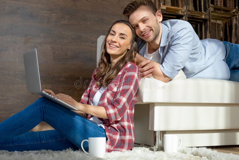 Couples utilisant l'ordinateur portable à la maison et souriant à l'appareil-photo photographie stock libre de droits Couples utilisant l'ordinateur portable à la maison et souriant à l'appareil-photo photographie stock libre de droits