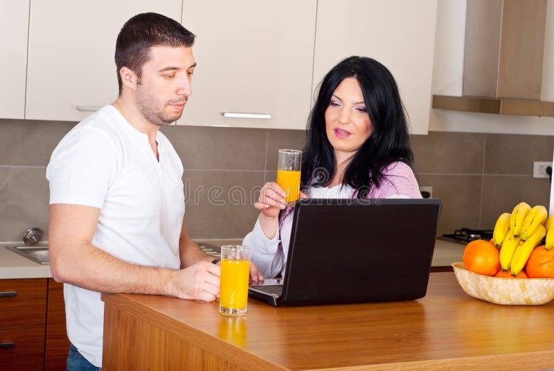 Couples utilisant l'ordinateur portatif dans leur cuisine photos libres de droits Couples utilisant l'ordinateur portatif dans leur cuisine photos libres de droits