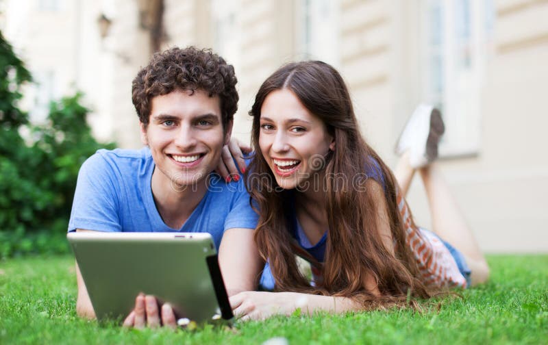 Couples utilisant le comprimé numérique sur la pelouse image libre de droits Couples utilisant le comprimé numérique sur la pelouse image libre de droits