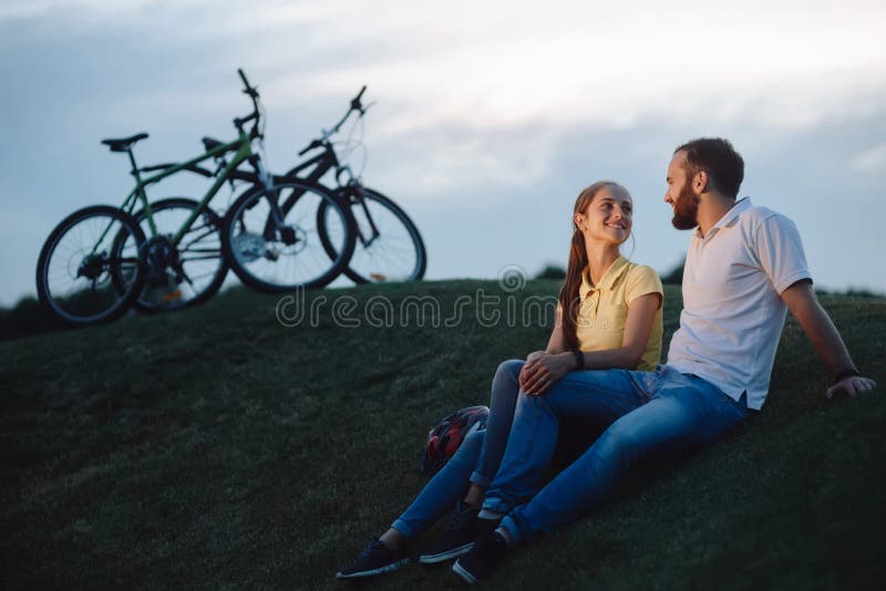 Couplez des cyclistes dans l'amour se reposant sur la colline verte image stock Couplez des cyclistes dans l'amour se reposant sur la colline verte image stock