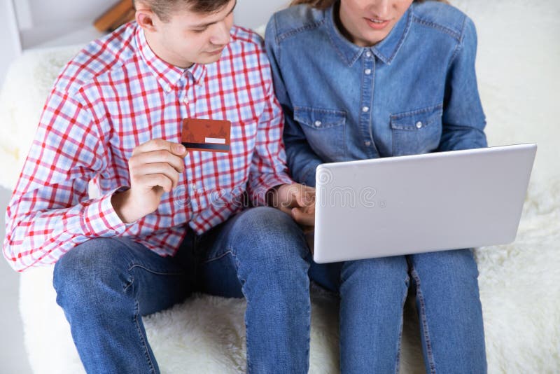 Couplez faire la séance en ligne de achat à la maison au sofa et employer la carte de crédit photo stock Couplez faire la séance en ligne de achat à la maison au sofa et employer la carte de crédit photo stock