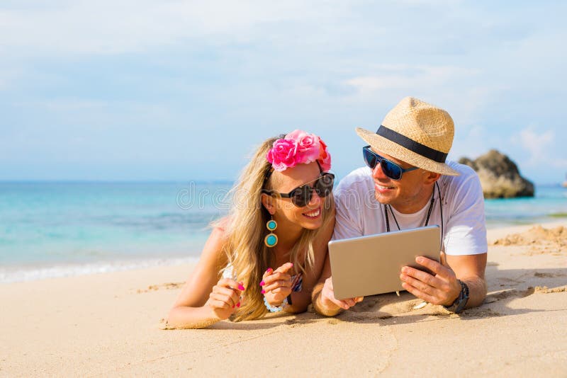 Couplez la détente sur la plage et regarder la tablette photos libres de droits Couplez la détente sur la plage et regarder la tablette photos libres de droits