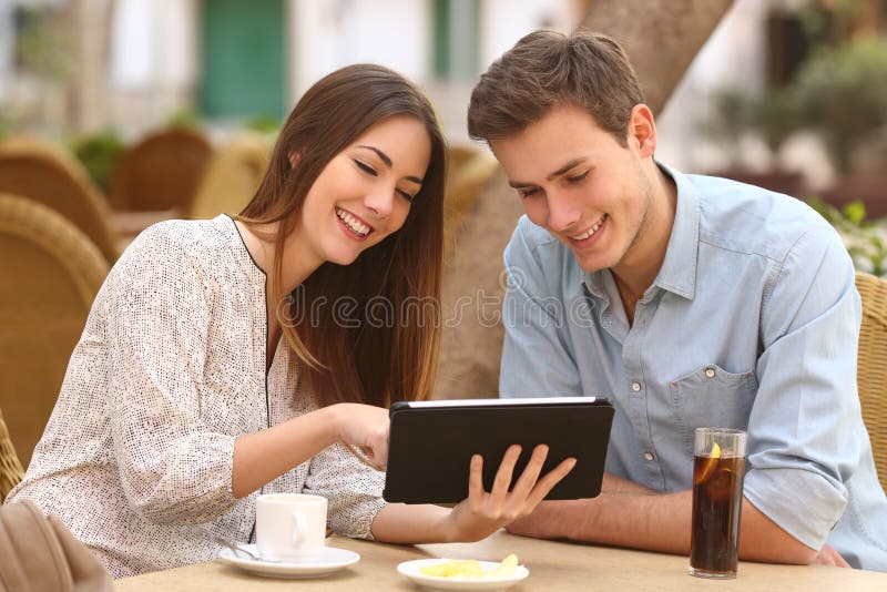 Happy couple watching media in a tablet in a restaurant terrace. Happy couple watching media in a tablet in a restaurant terrace