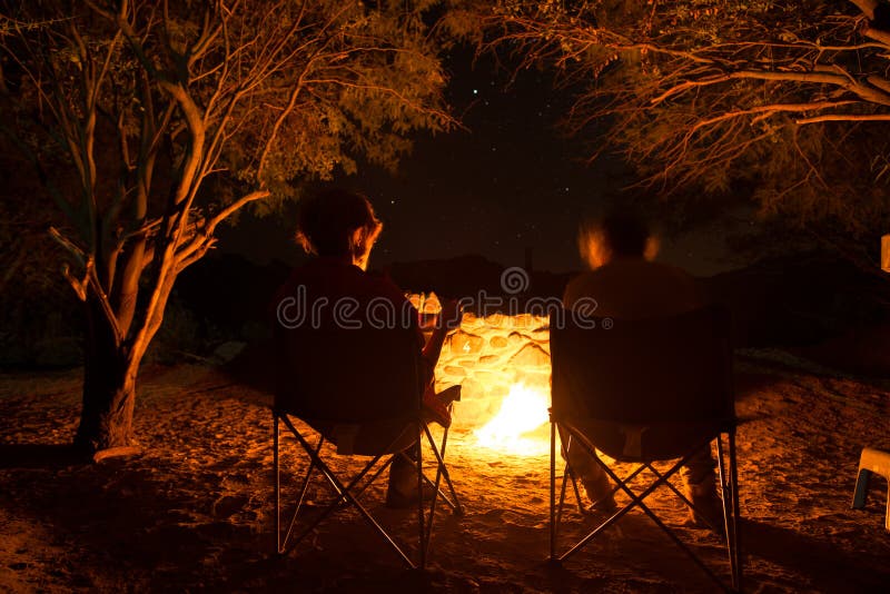 Couplez se reposer au feu brûlant de camp pendant la nuit Campant dans la forêt sous le ciel étoilé, la Namibie, Afrique Aventure image libre de droits Couplez se reposer au feu brûlant de camp pendant la nuit Campant dans la forêt sous le ciel étoilé, la Namibie, Afrique Aventure image libre de droits