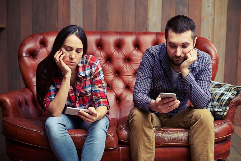 Couplez se reposer sur le divan regardant leurs téléphones photos stock Couplez se reposer sur le divan regardant leurs téléphones photos stock