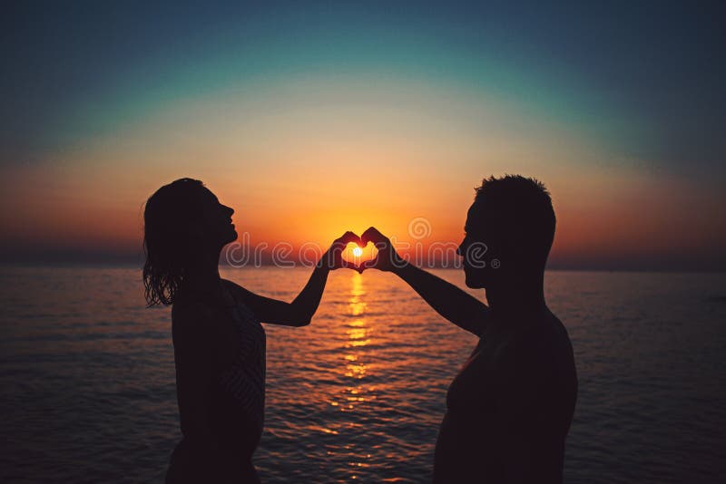 Couplez sur la plage de coucher du soleil à la station de vacances tropicale pour faire le coeur à partir des mains voyagent conc photo stock Couplez sur la plage de coucher du soleil à la station de vacances tropicale pour faire le coeur à partir des mains voyagent conc photo stock