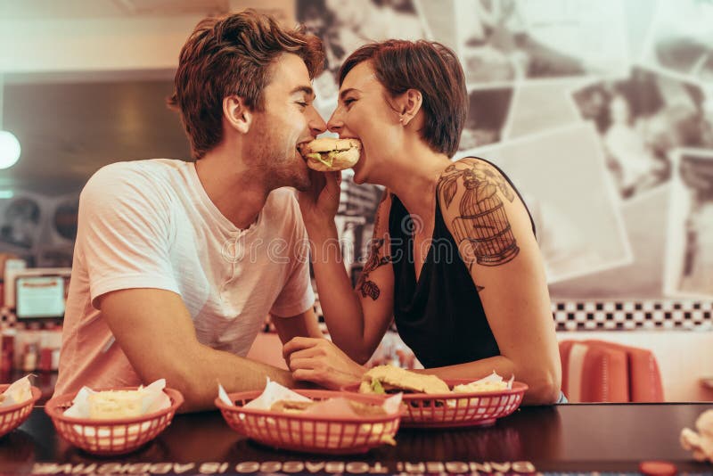 Coupé nell'umore romantico che divide un hamburger ad un ristorante