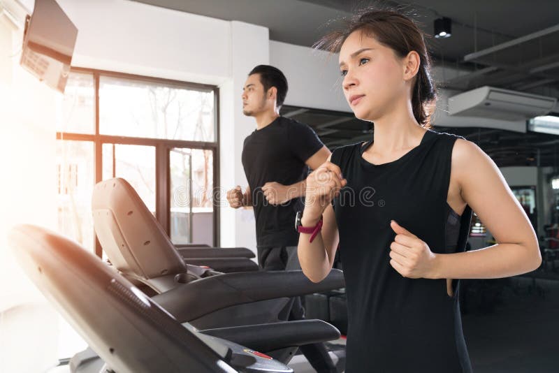 Courant sur les tapis roulants, la jeune femme active et l'homme courant sur le tapis roulant dans le gymnase photographie stock Courant sur les tapis roulants, la jeune femme active et l'homme courant sur le tapis roulant dans le gymnase photographie stock