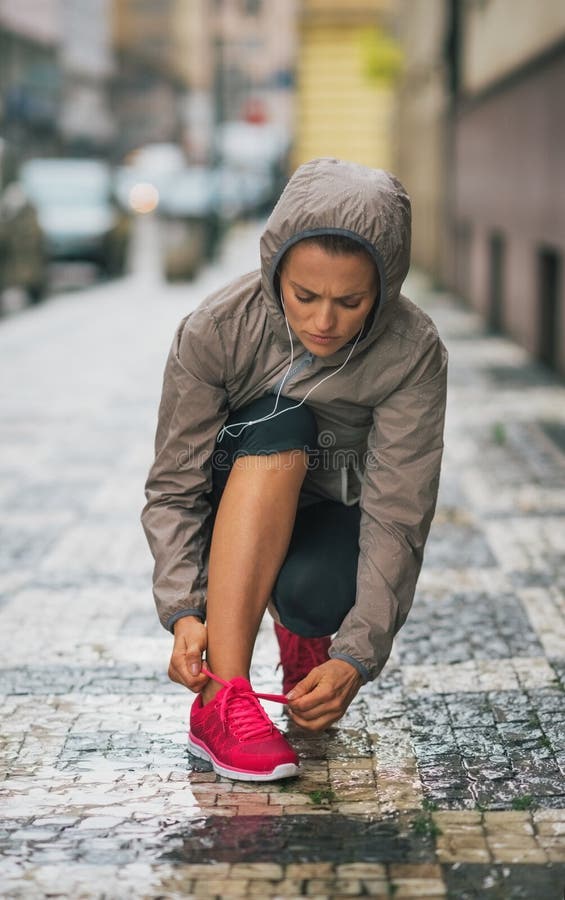 Coureur de femme se mettant à genoux vers le bas pour attacher la chaussure de course sous la pluie photographie stock libre de droits