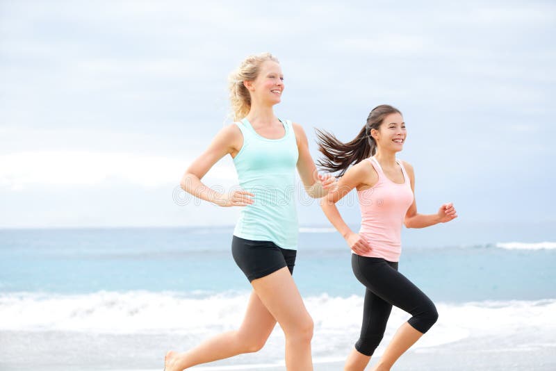 Runners - two women running outdoors training. Exercising female athletes jogging outside on beach smiling happy. Multiracial Asian and Caucasian women in healthy lifestyle. Runners - two women running outdoors training. Exercising female athletes jogging outside on beach smiling happy. Multiracial Asian and Caucasian women in healthy lifestyle.